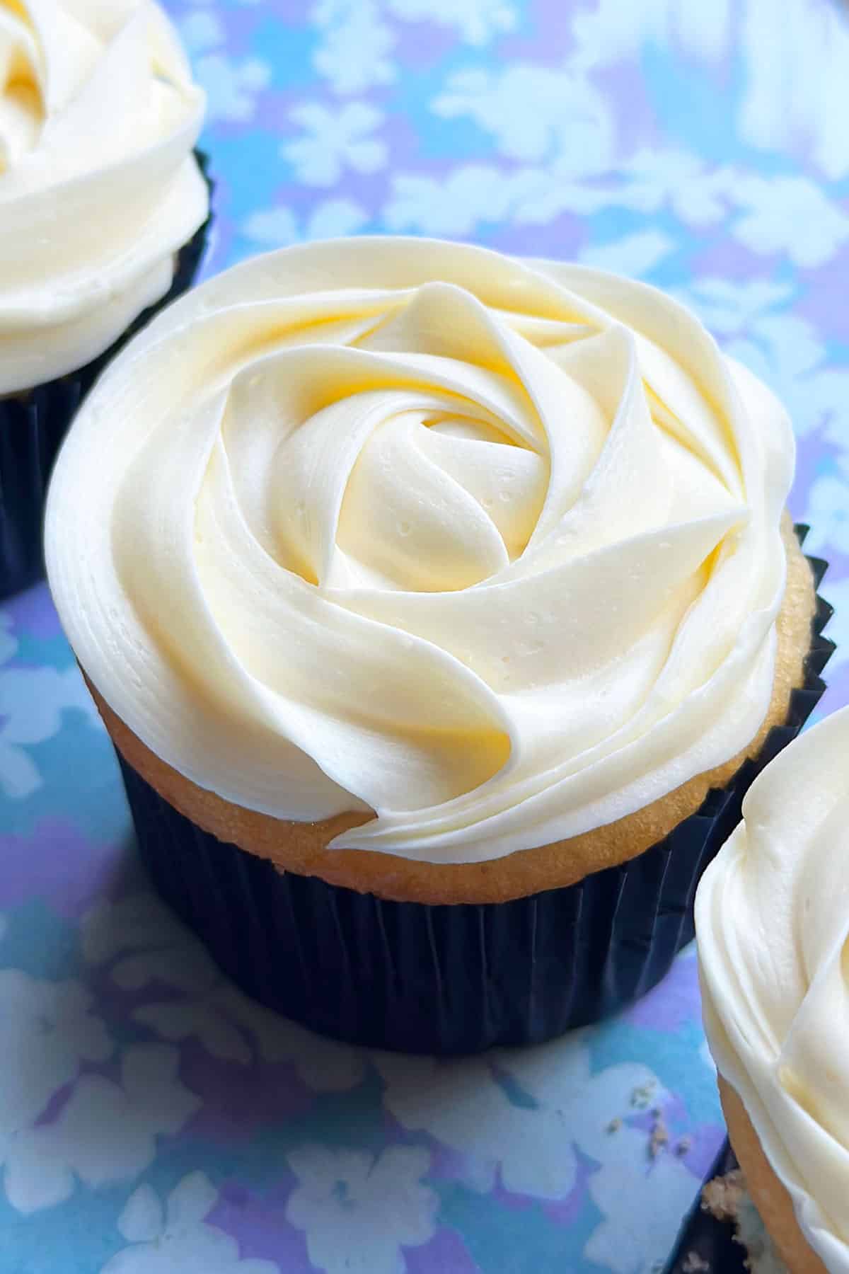 Easy Almond Buttercream Frosting Piped on Top of Cupcake on Blue Background.