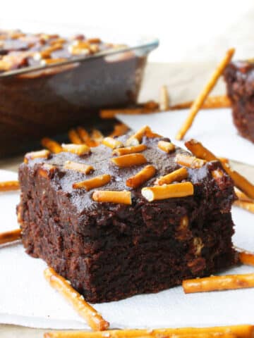 Slice of Easy Fudgy Chocolate Cake Mix Brownies With Ganache and Pretzels on White Napkin.