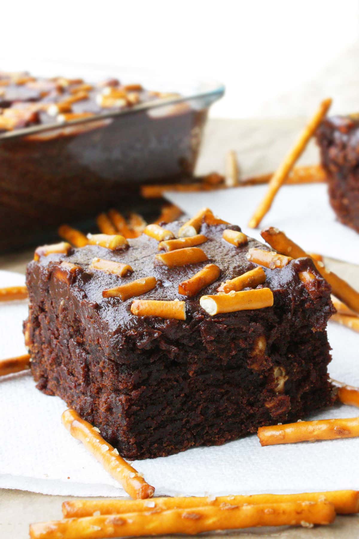 Slice of Easy Fudgy Chocolate Cake Mix Brownies With Ganache and Pretzels on White Napkin. 