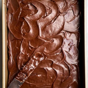 Chocolate Sour Cream Frosting Spread on Top of Rectangular Cake With Spatula on the Side.