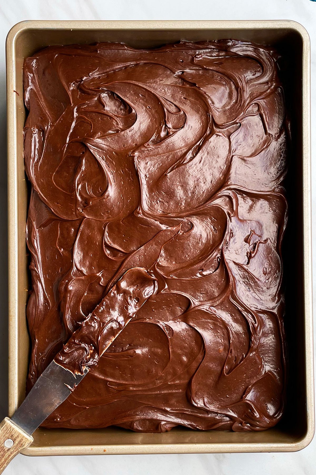 Chocolate Sour Cream Frosting Spread on Top of Rectangular Cake With Spatula on the Side. 