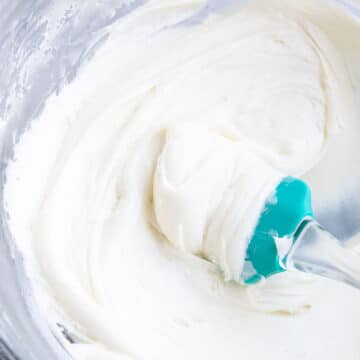 Easy Vanilla Sour Cream Frosting in Glass Bowl With Green Rubber Spatula.