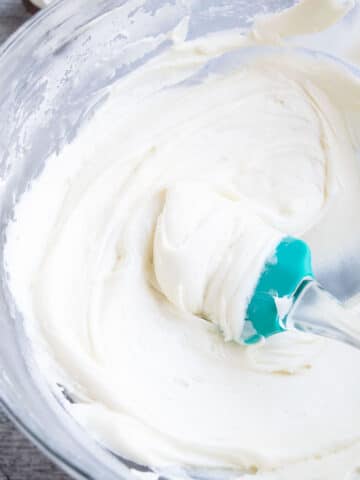 Easy Vanilla Sour Cream Frosting in Glass Bowl With Green Rubber Spatula.