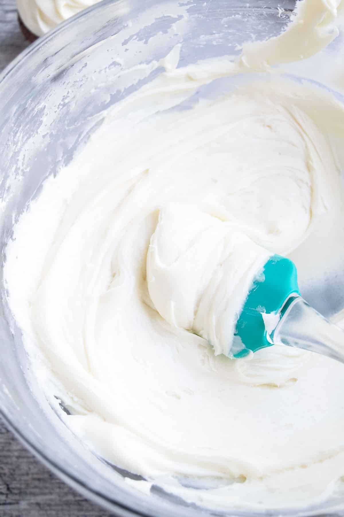 Easy Vanilla Sour Cream Frosting in Glass Bowl With Green Rubber Spatula. 