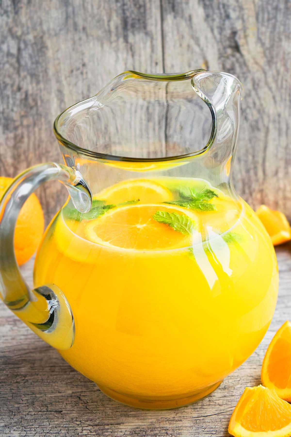 Glass Jug Full of Orange Lemonade on Rustic Gray Background. 