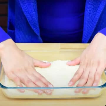 Spreading Coconut Mixture Layer in Glass Dish and Pressing Down With Hands. 