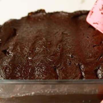Brownie batter being spread in square dish. 