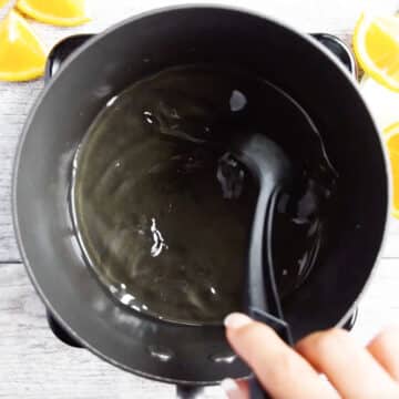 Sugar syrup being mixed with a spoon in nonstick pot. 