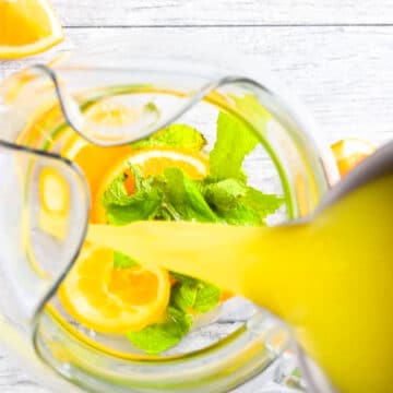 Pouring citrus lemonade in glass pitcher. 