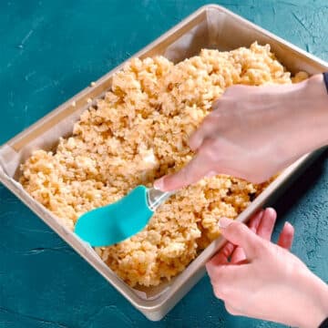Sticky rice krispies mixture being spread in a rectangle pan with rubber spatula. 