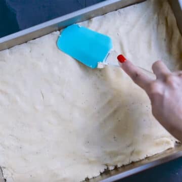 Batter being spread in baking pan with rubber spatula. 