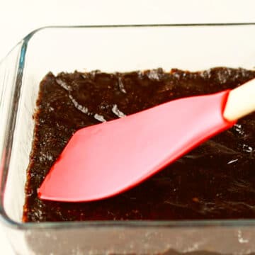 Sticky date mixture being spread in glass pan. 