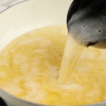 Apple cider being poured in large nonstick pot. 