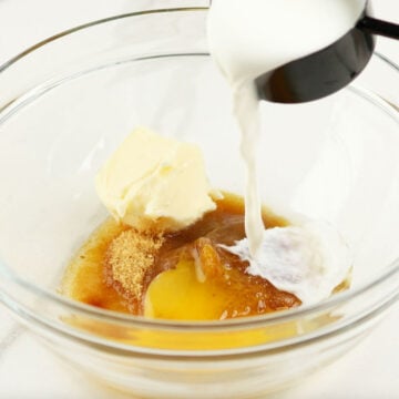 Milk being poured in glass bowl with eggs, butter, sugar and vanilla. 