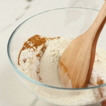 Wooden spoon being used to mix flour, spices and leavening agents in glass bowl. 