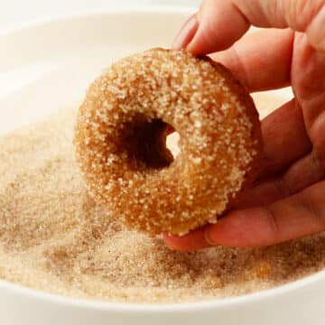 Donuts getting covered in cinnamon sugar mixture. 