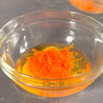 Glass mixing bowl with eggs, water, oil and shredded carrots. 