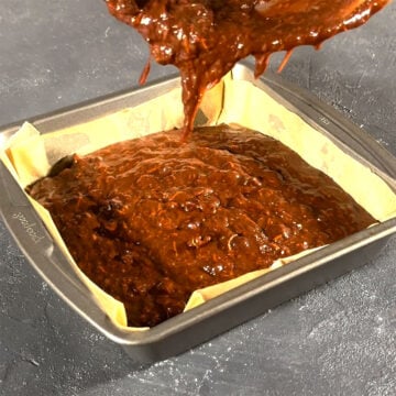 Brownie batter being poured in a lined square pan. 