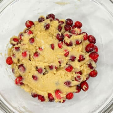 Fresh cranberries folded into batter in glass bowl. 