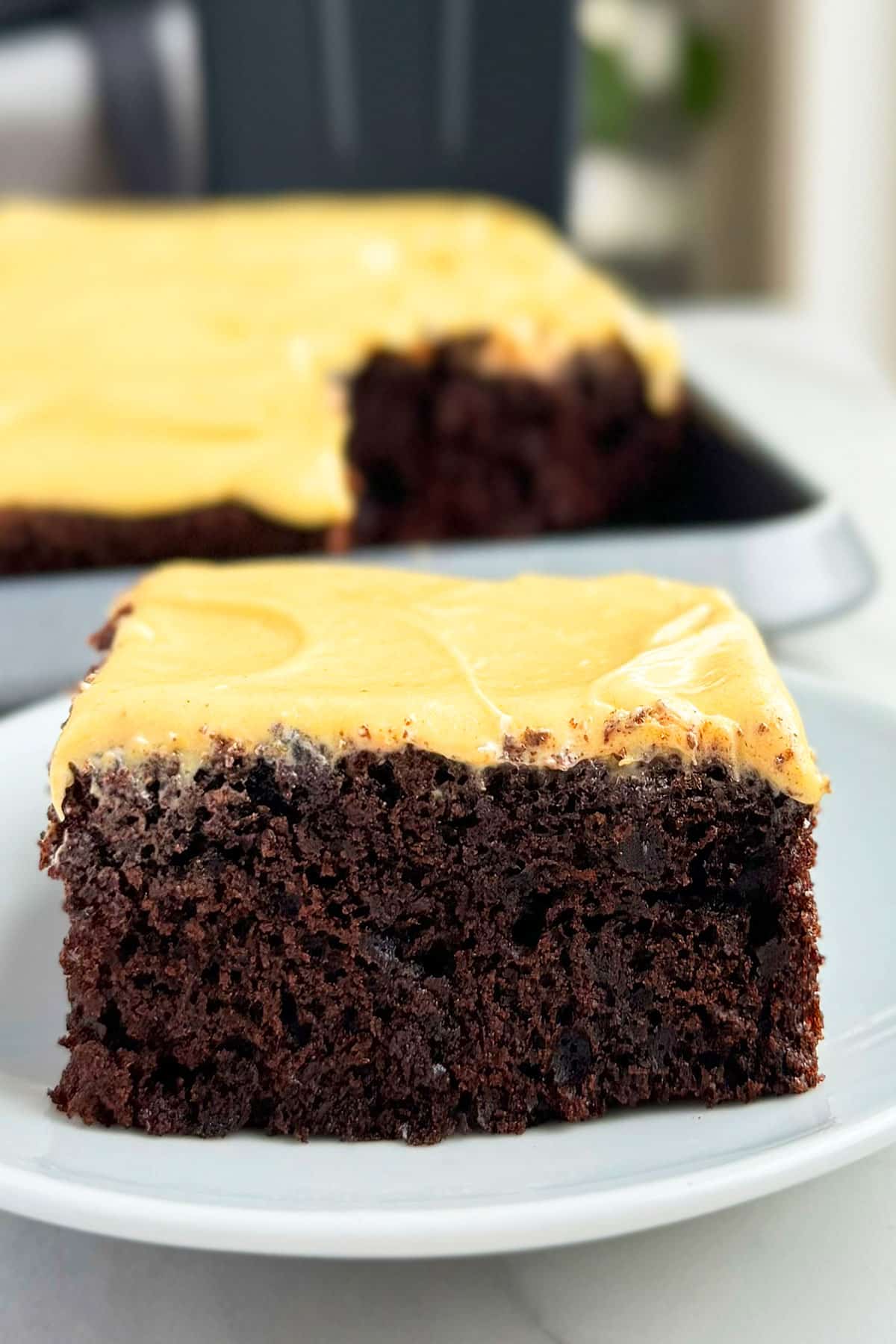 Slice of Easy Chocolate Pumpkin Cake With Pumpkin Cream Cheese Frosting on White Dish.