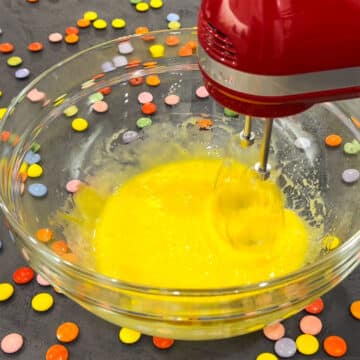 Eggs and oil being mixed in glass bowl on black stone background. 