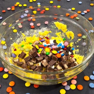 Chopped candies added to dough in glass bowl. 