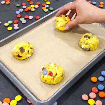 Cookie dough balls being placed on a baking tray. 