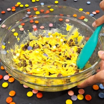 Candies being mixed into dough with turquoise spoon in glass bowl. 