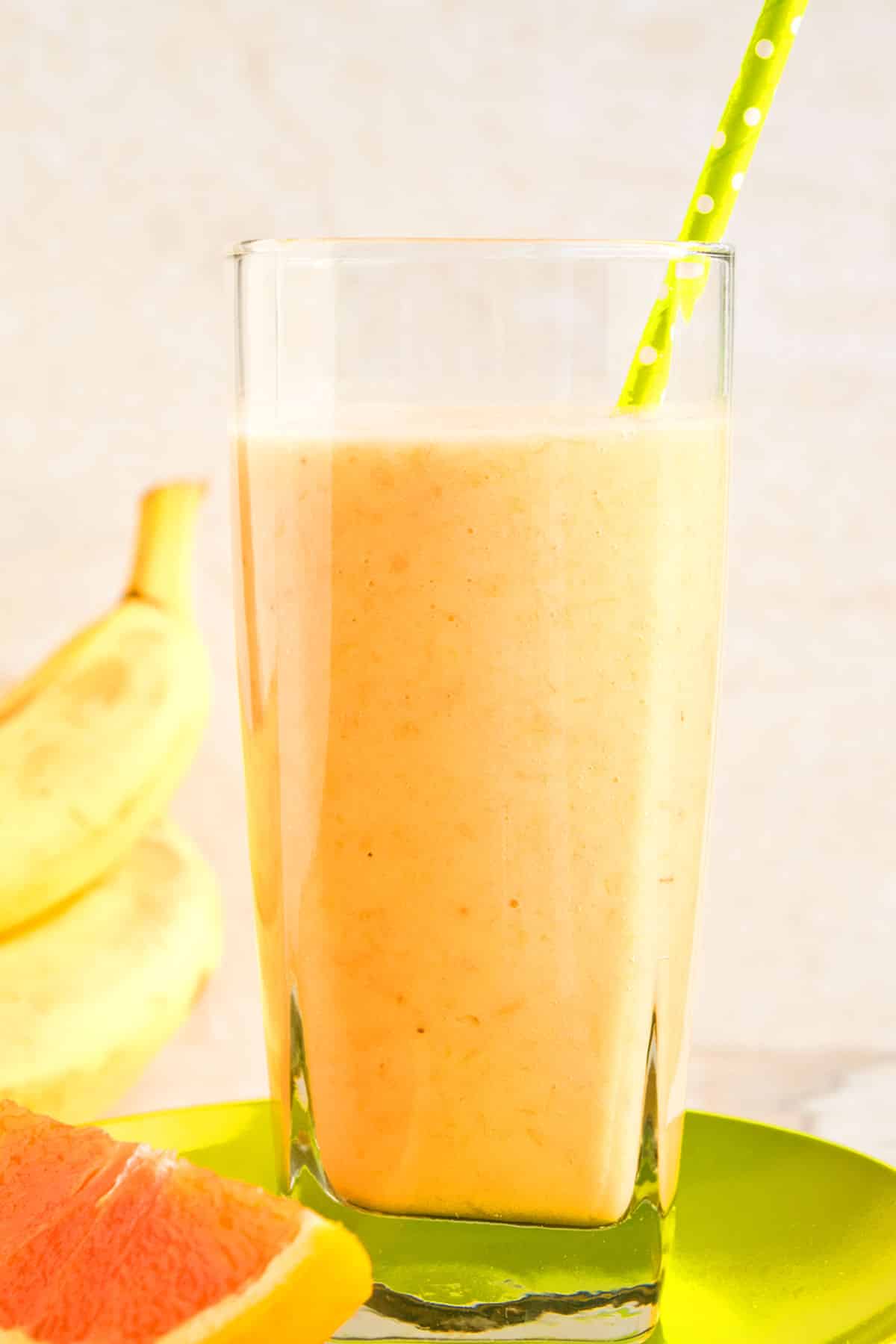 Easy Orange Banana Mango Smoothie in Glass Cup With Green Polka Dot Straw. 