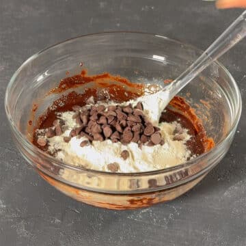 Glass bowl with chocolate mixture, flour, chocolate chips. 