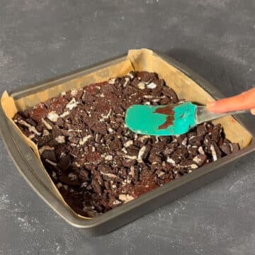 Brownie batter being pressed with crushed cookies using a spatula. 