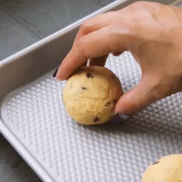 Cookie dough ball being placed on a baking tray. 