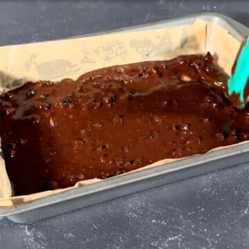 Brownie batter being spread evenly in a lined baking pan. 