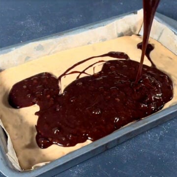 Brownie batter being poured on top of caramel layer. 