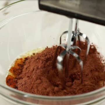 Large glass bowl with butter, sugar, cocoa powder, vanilla extract, eggs.