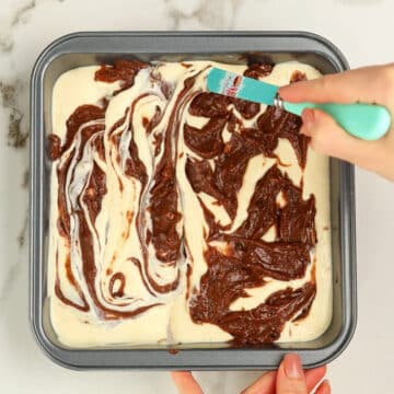 Butter knife being used to make swirls of chocolate batter and cream cheese mixture. 