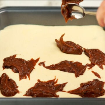 Spoonfuls of chocolate batter being dropped on top of cheesecake mixture. 