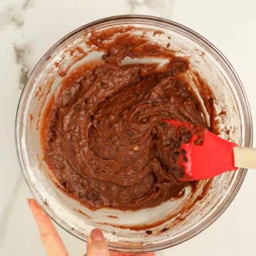 Chocolate chips being stirred into brownie batter. 