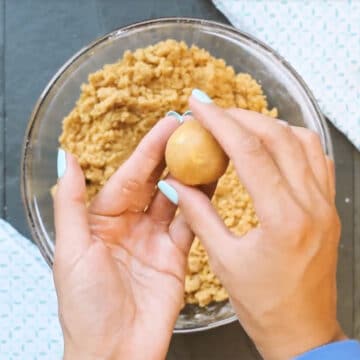 Cookie dough balls being formed with hands. 