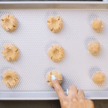 Cookie dough balls being indented in the center before baking. 