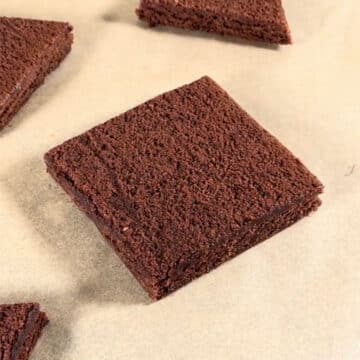 Square brownie slice on brown parchment paper. 