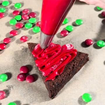 Piping red frosting on top of triangle brownie. 