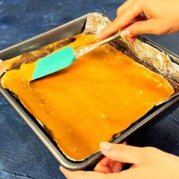 Melted caramel being spread on top of baked cookie base. 