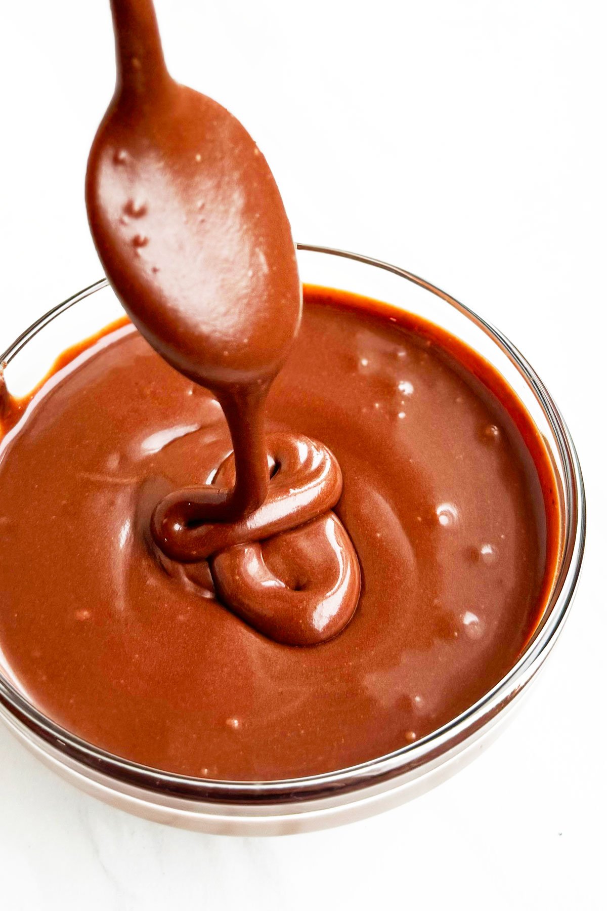 Spoonful of Cocoa Powder Glaze Being Drizzled in Glass Bowl. 