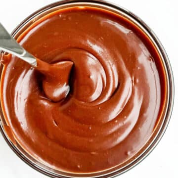 Glass Bowl Full of Chocolate Glaze For Cakes and Donuts With a Silver Spoon.