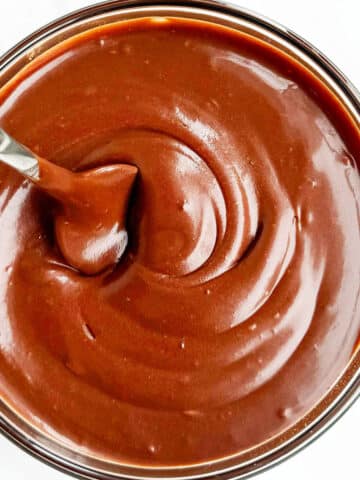 Glass Bowl Full of Chocolate Glaze For Cakes and Donuts With a Silver Spoon.