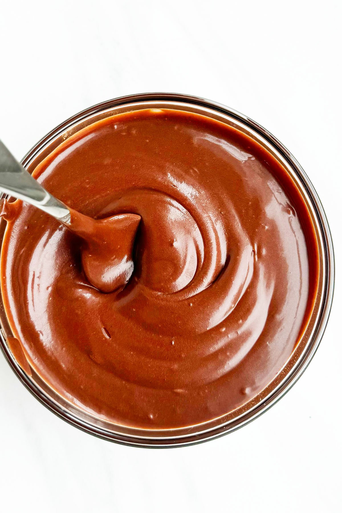 Glass Bowl Full of Chocolate Glaze For Cakes and Donuts With a Silver Spoon. 