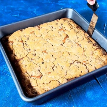 Baked brownie cookie hybrid in baking pan with sides being loosened using an offset spatula. 