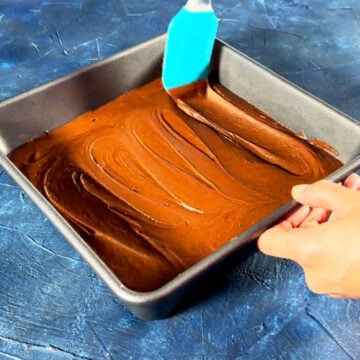 Brownie batter being spread with rubber spatula in baking pan. 