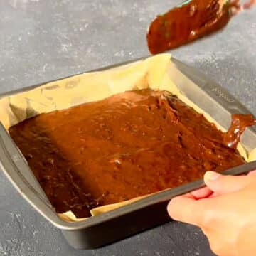 Brownie batter spread out in baking pan with a spatula. 